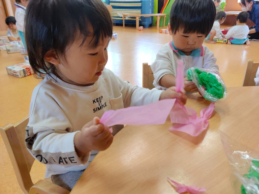 花紙をぎゅっと握って、ちぎれる感触に夢中のすみれ組さん(1歳児クラス)