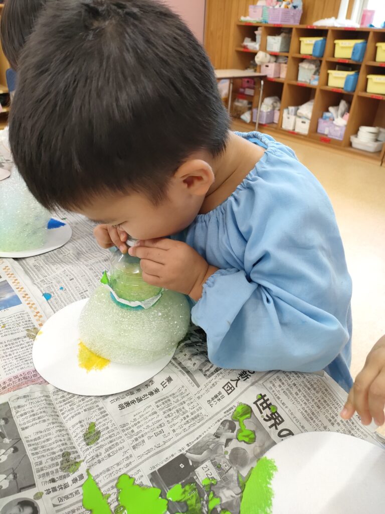 ストローで色付きの泡を吹き上げる、うめ組さん(3歳児クラス)の真剣な表情