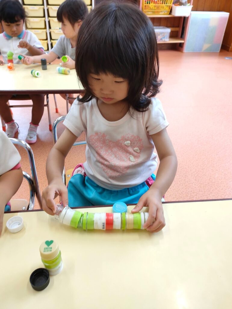 ペットボトルの蓋を長くつなげて、うれしそうに見せに来るいちご組さん(2歳児クラス)