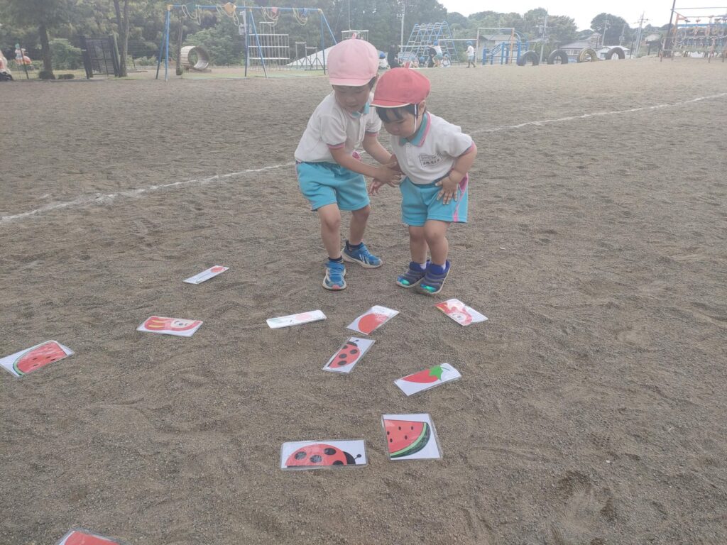 「こっちだよ」— カードを指さすさくら組さんと、見つめるうめ組(3歳児クラス)さん
