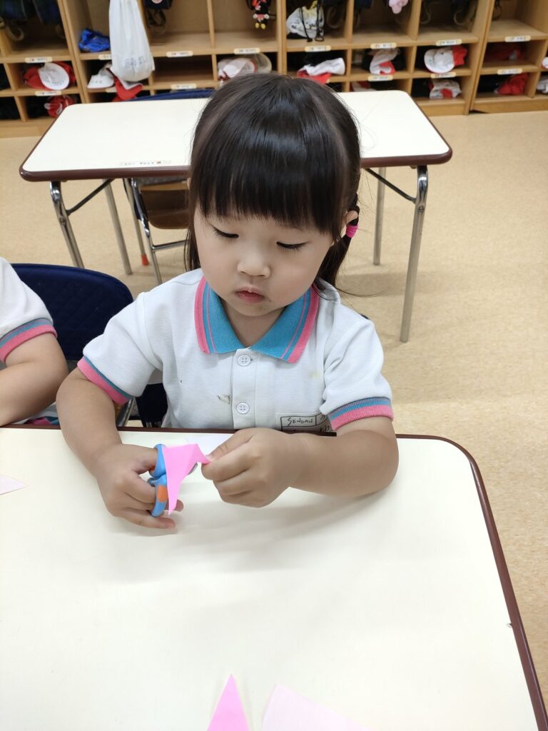 線の上をはさみで二回切り。折り紙をしっかり持って進めるうめ組さん(3歳児クラス)の職人ぶり