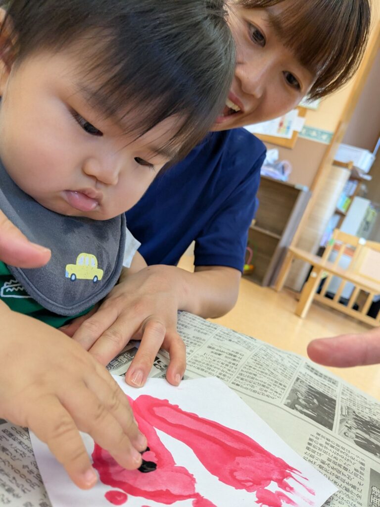 赤い絵の具に指先でそっと触れるひよこ組さん(0歳児クラス)