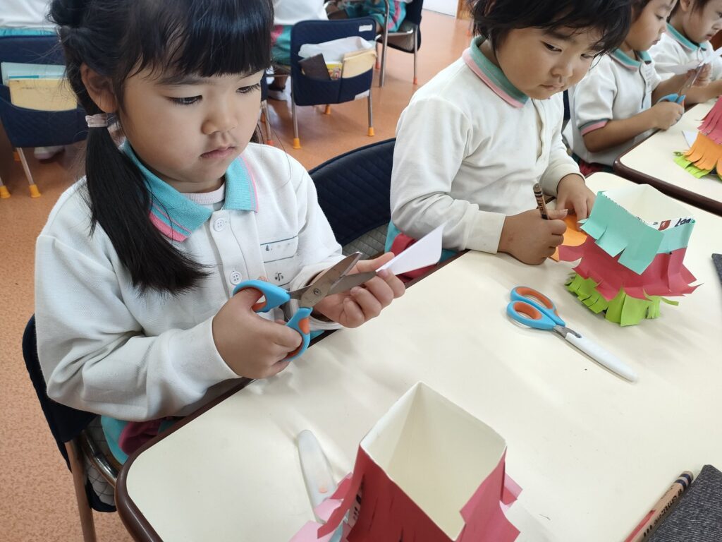 友だちの手元をのぞきこみながら作るもも組さん(4歳児クラス)